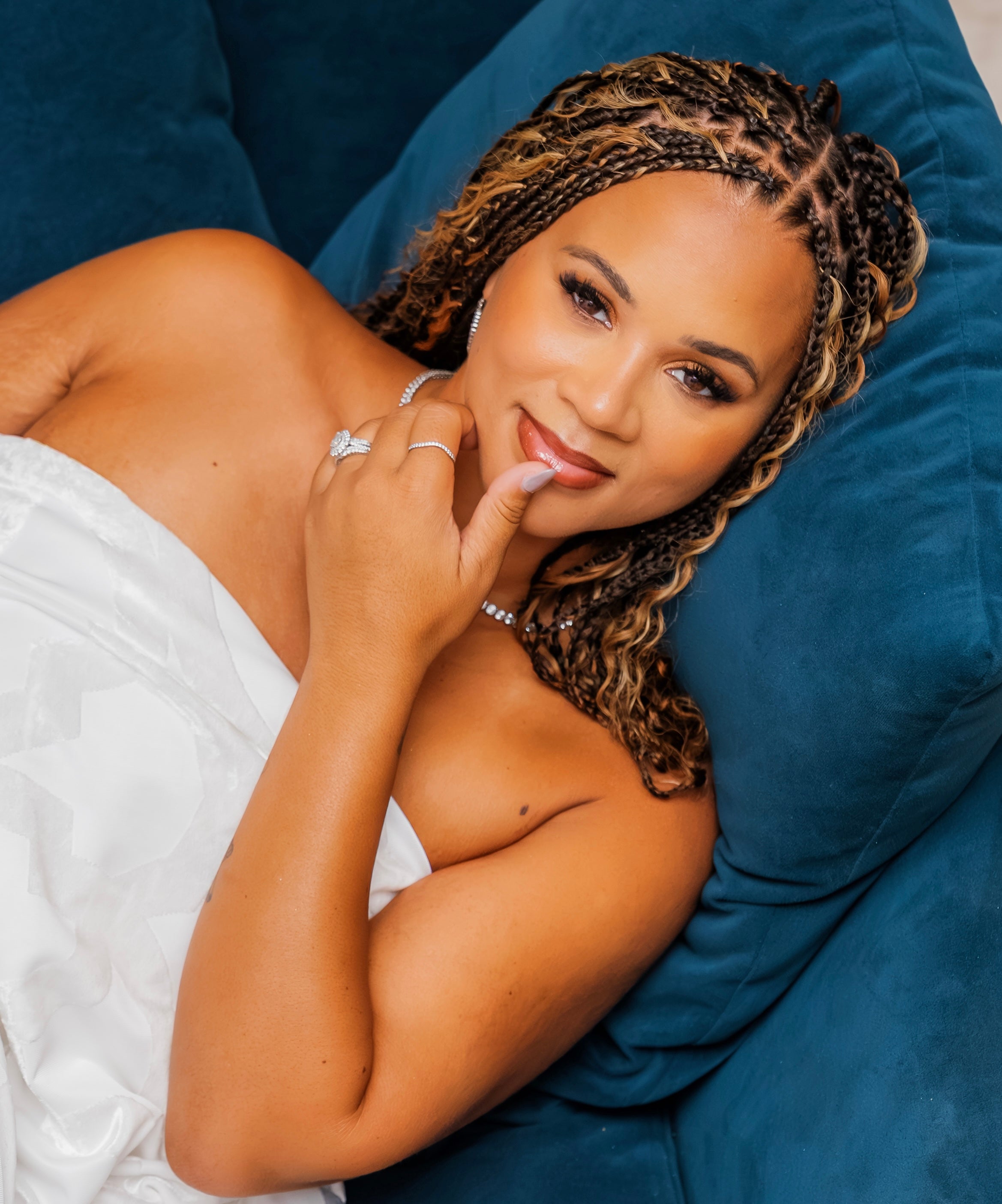 Woman with braided hair lying on a blue pillow wearing a white top.
